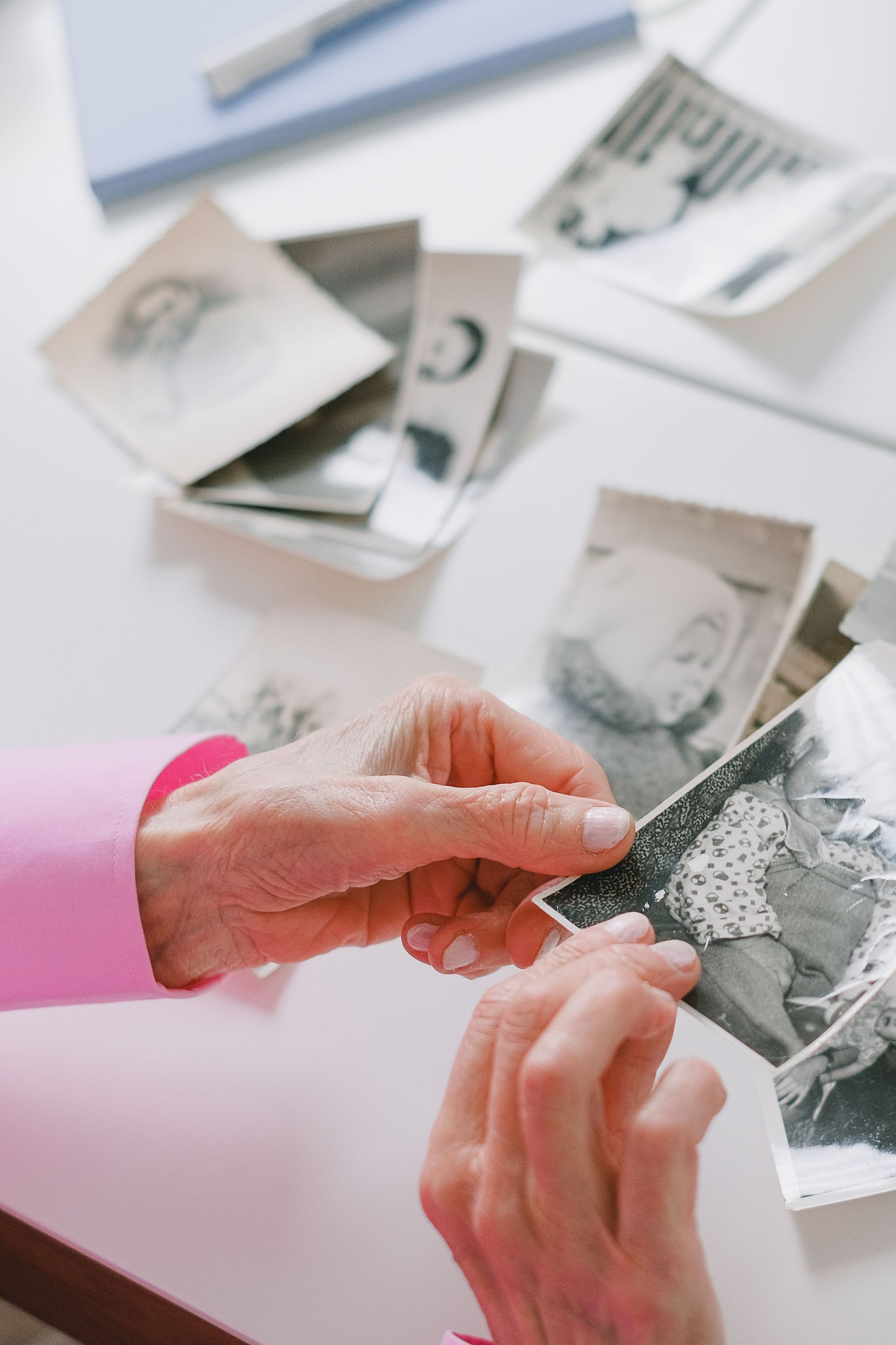 An elderly person with pink sleeves is reviewing nostalgic black and white photographs at a table.